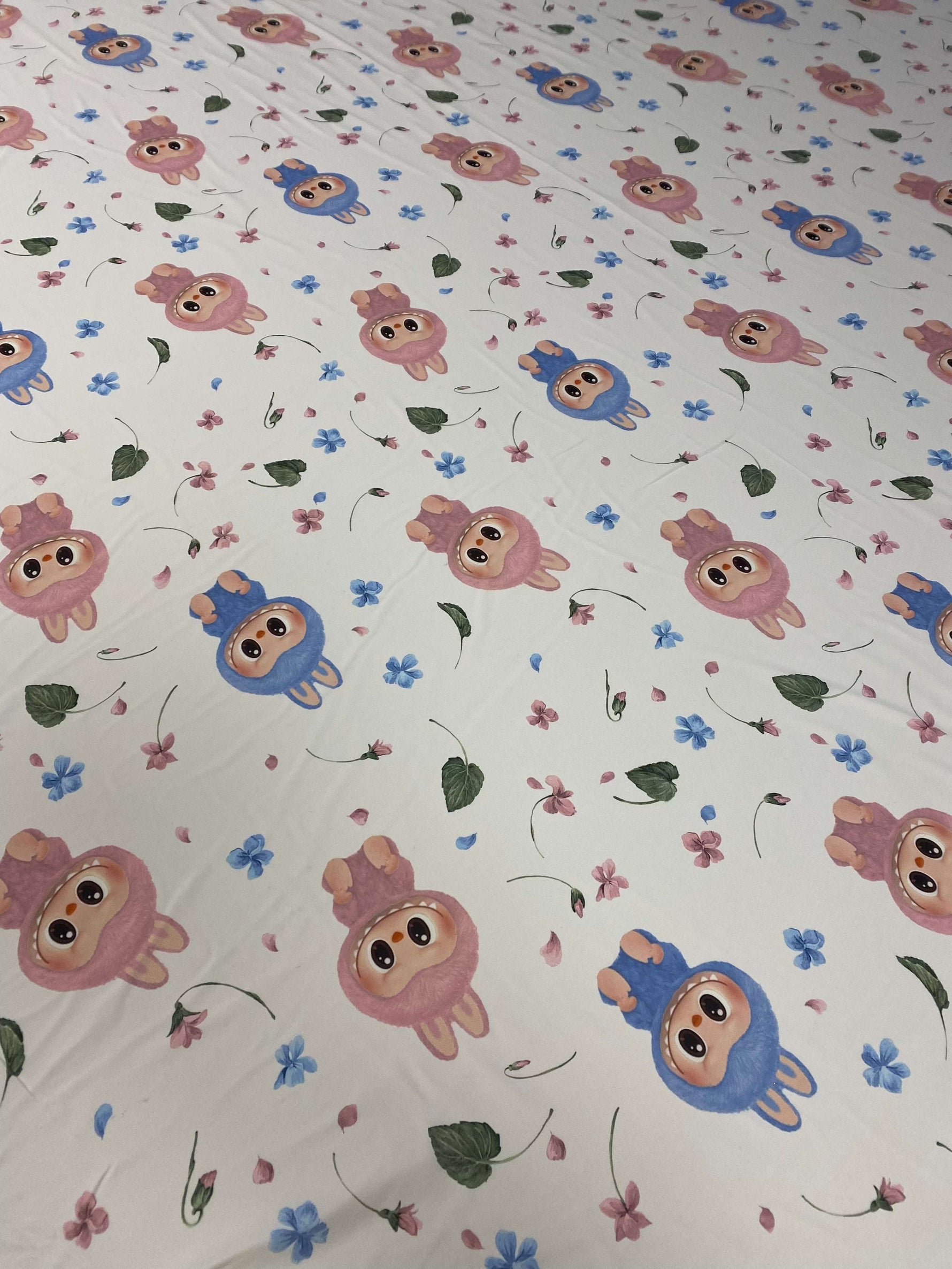Cute cartoon animal print fabric with pink and blue characters and small floral accents on a white background