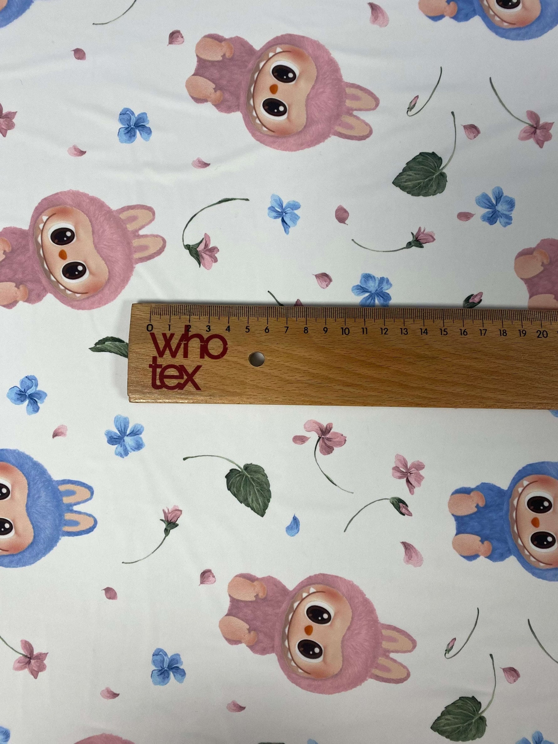 Cute cartoon animal print fabric with pink and blue animal characters and scattered floral accents, shown with a ruler for scale