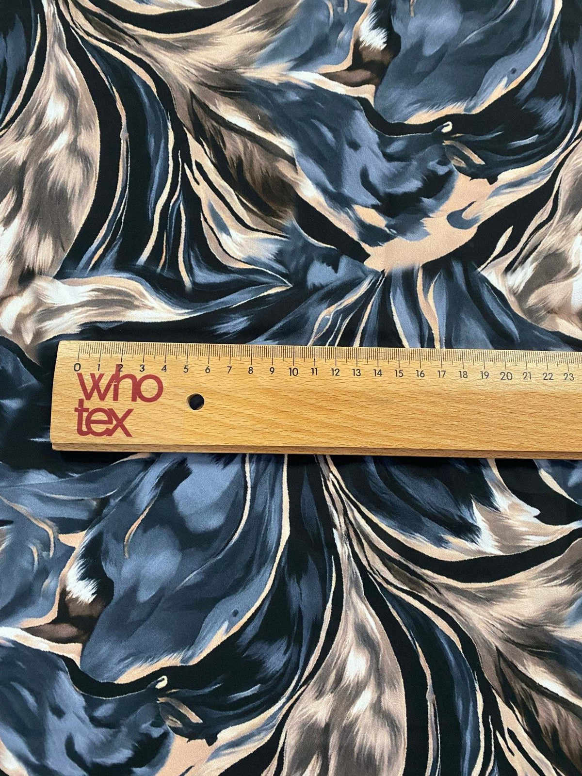 Close-up of abstract feather pattern fabric in black, beige, and blue with ruler for scale