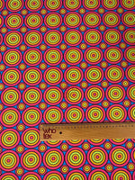 Colorful geometric circles print fabric with vibrant concentric circles in red, yellow, green, and blue, shown with a wooden ruler for scale