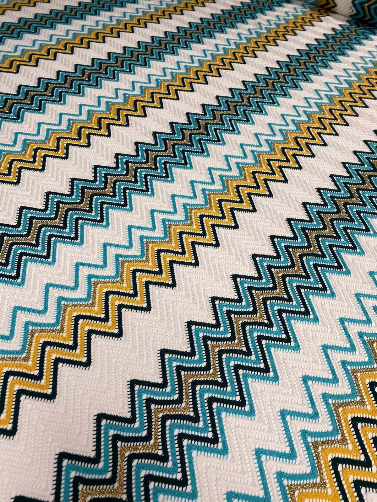 Close-up of geometric zigzag embroidered fabric in green, teal, mustard, and white tones with intricate knit texture