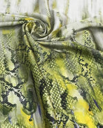 Green snake skin patterned fabric with textured surface and yellow and black hues, folded in a swirl.