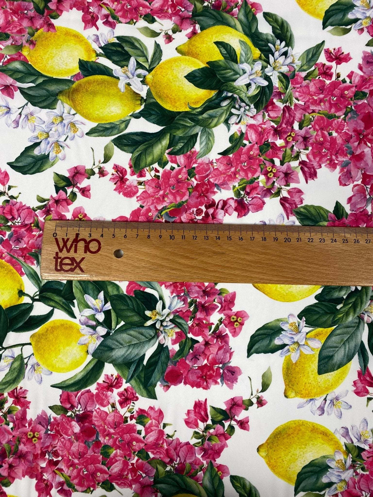close-up of lemon pink floral fabric with vibrant lemons and pink flowers alongside a wooden ruler showing fabric scale