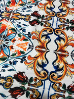 Close-up of colorful Majolica pattern fabric featuring ornate blue, orange, and green floral and scroll designs on white background