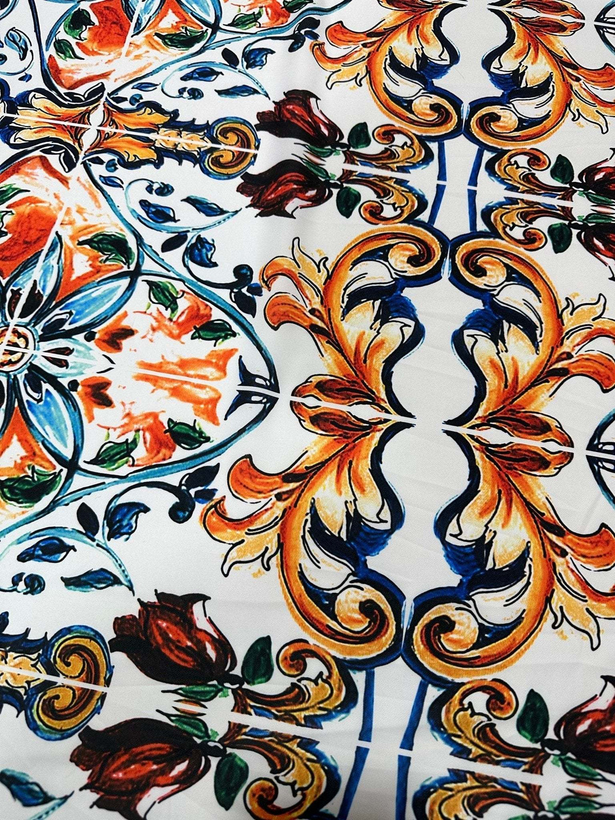 Close-up of colorful Majolica pattern fabric featuring ornate blue, orange, and green floral and scroll designs on white background