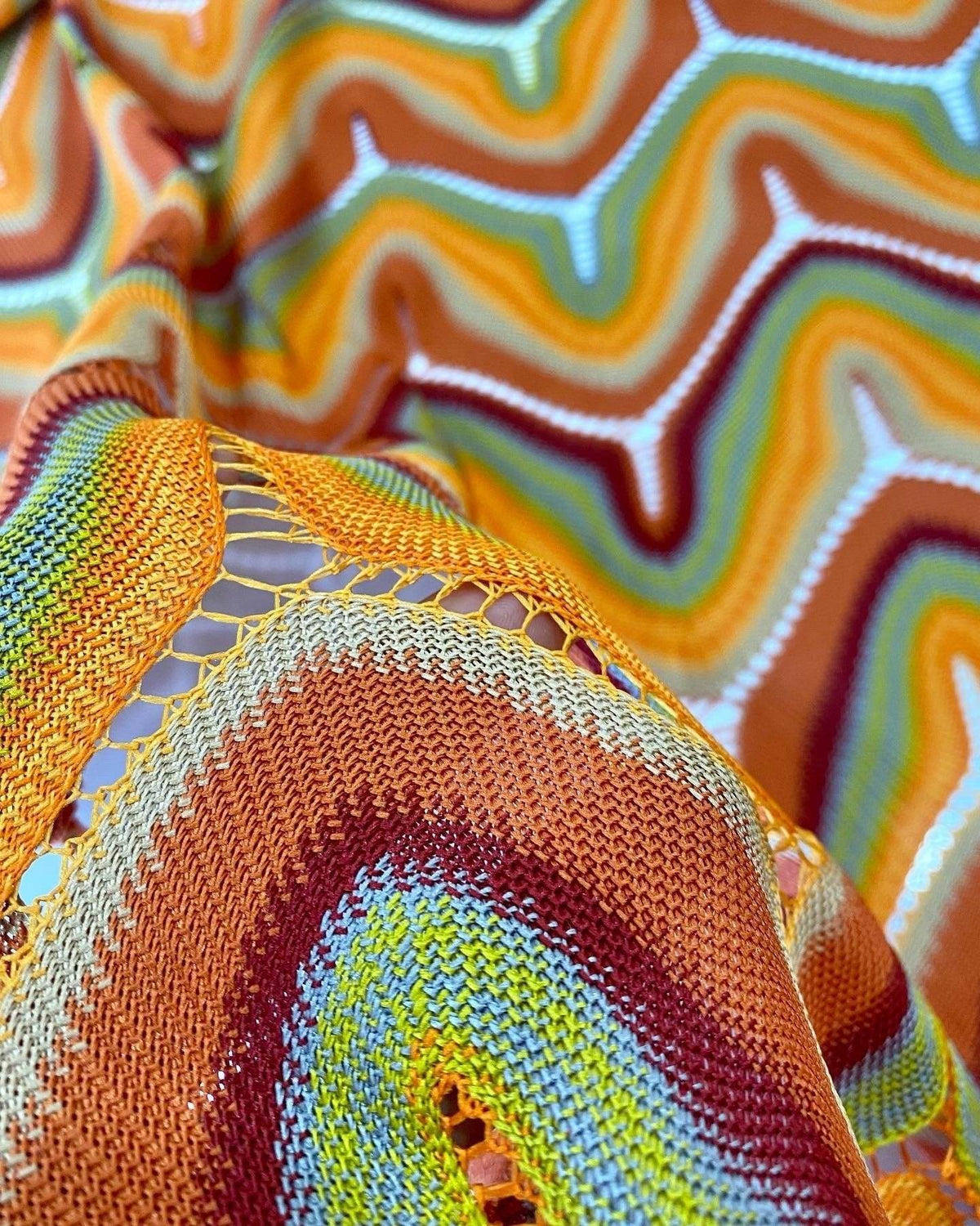 Close-up of zigzag knit jersey mesh fabric with multicolor orange, yellow, green, and brown pattern and textured knit details