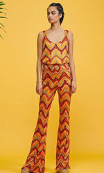 Woman wearing colorful zigzag knit jersey mesh fabric outfit with sleeveless top and flared pants on yellow background