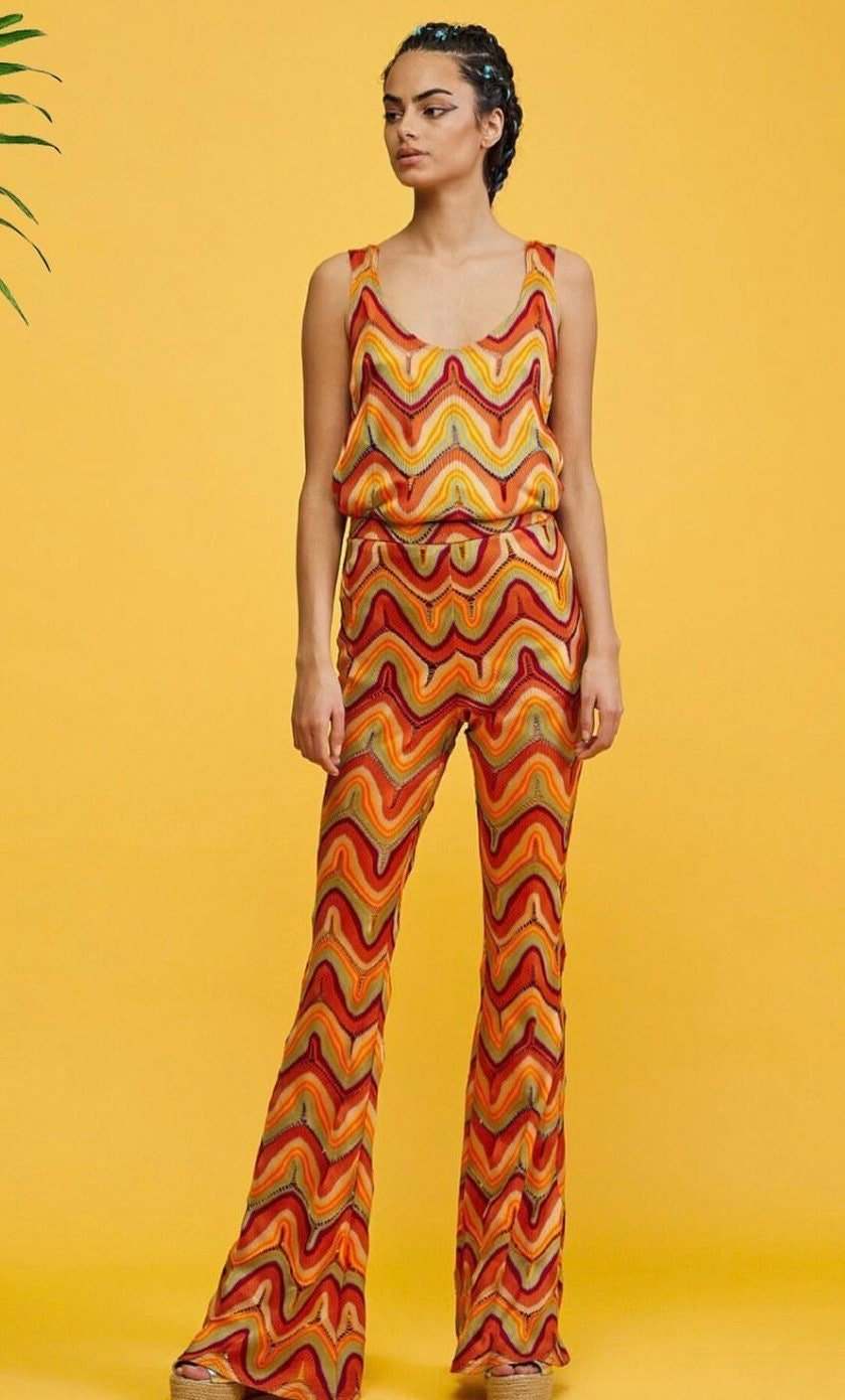 Woman wearing colorful zigzag knit jersey mesh fabric outfit with sleeveless top and flared pants on yellow background
