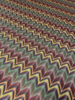 Multicolor chevron jacquard fabric with vibrant zigzag pattern in green, yellow, red, and black tones, ideal for sewing garments.