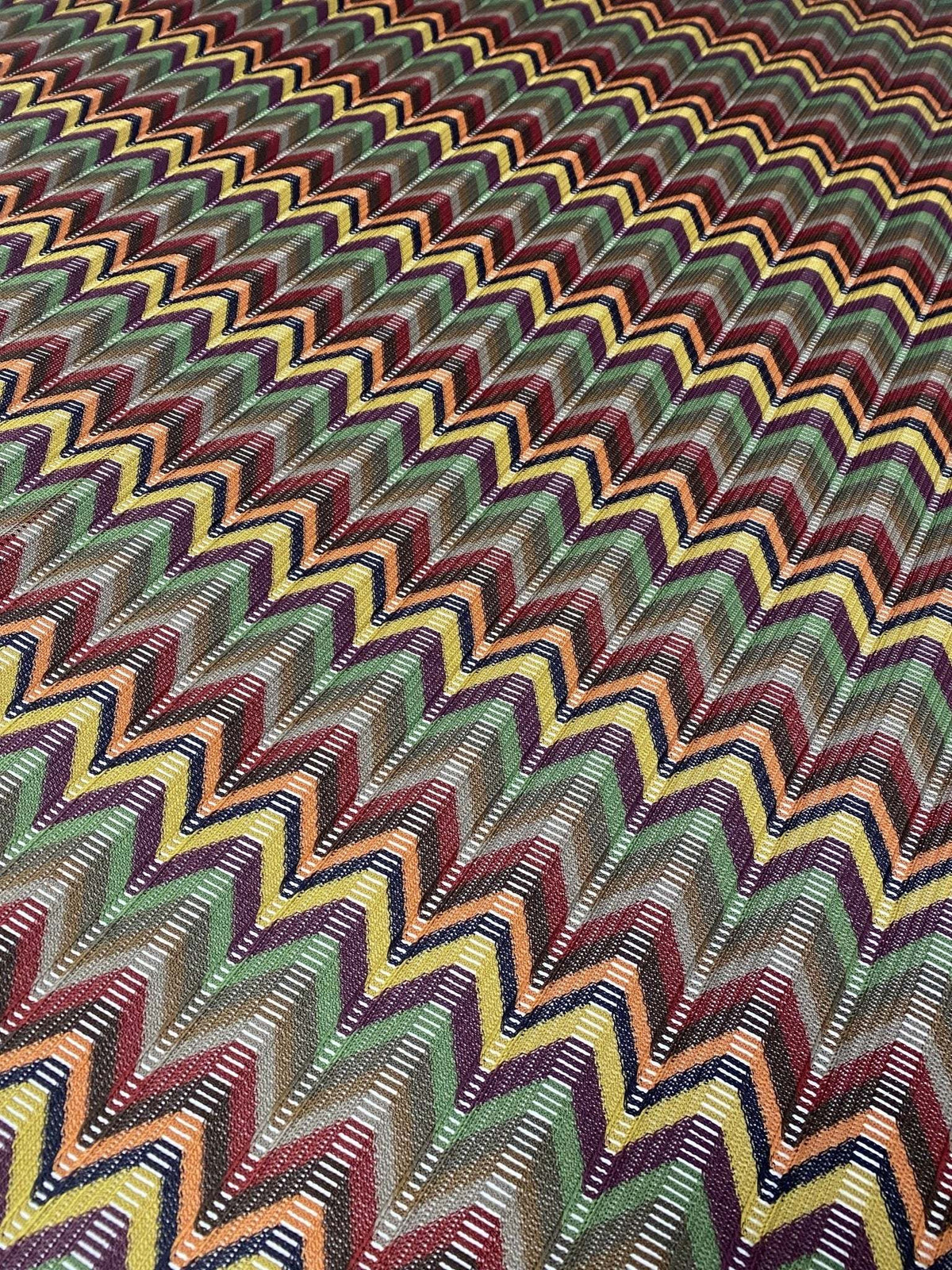 Multicolor chevron jacquard fabric with vibrant zigzag pattern in green, yellow, red, and black tones, ideal for sewing garments.