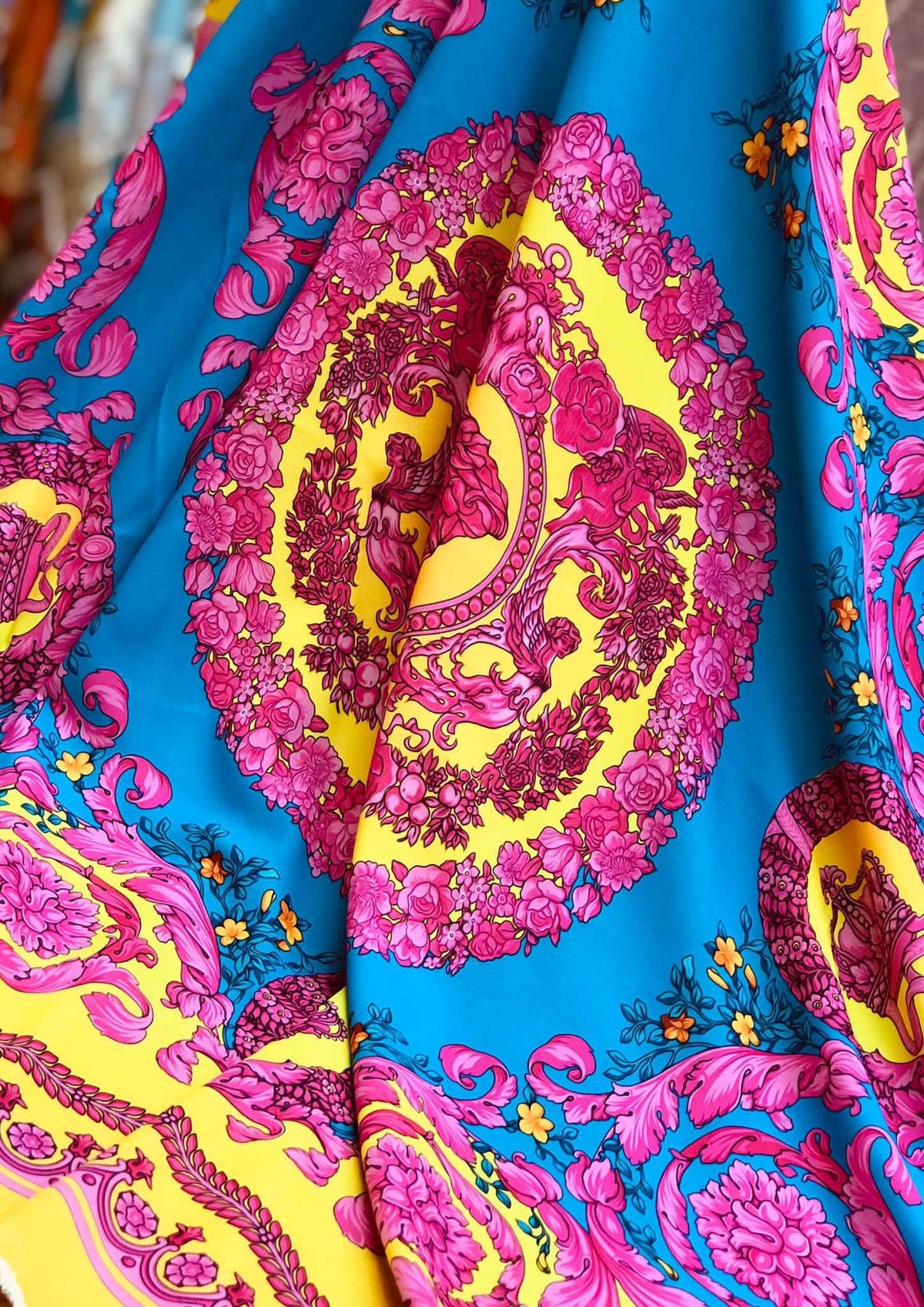 vibrant pink baroque silky fabric with intricate floral and cherub patterns on bright blue and yellow background
