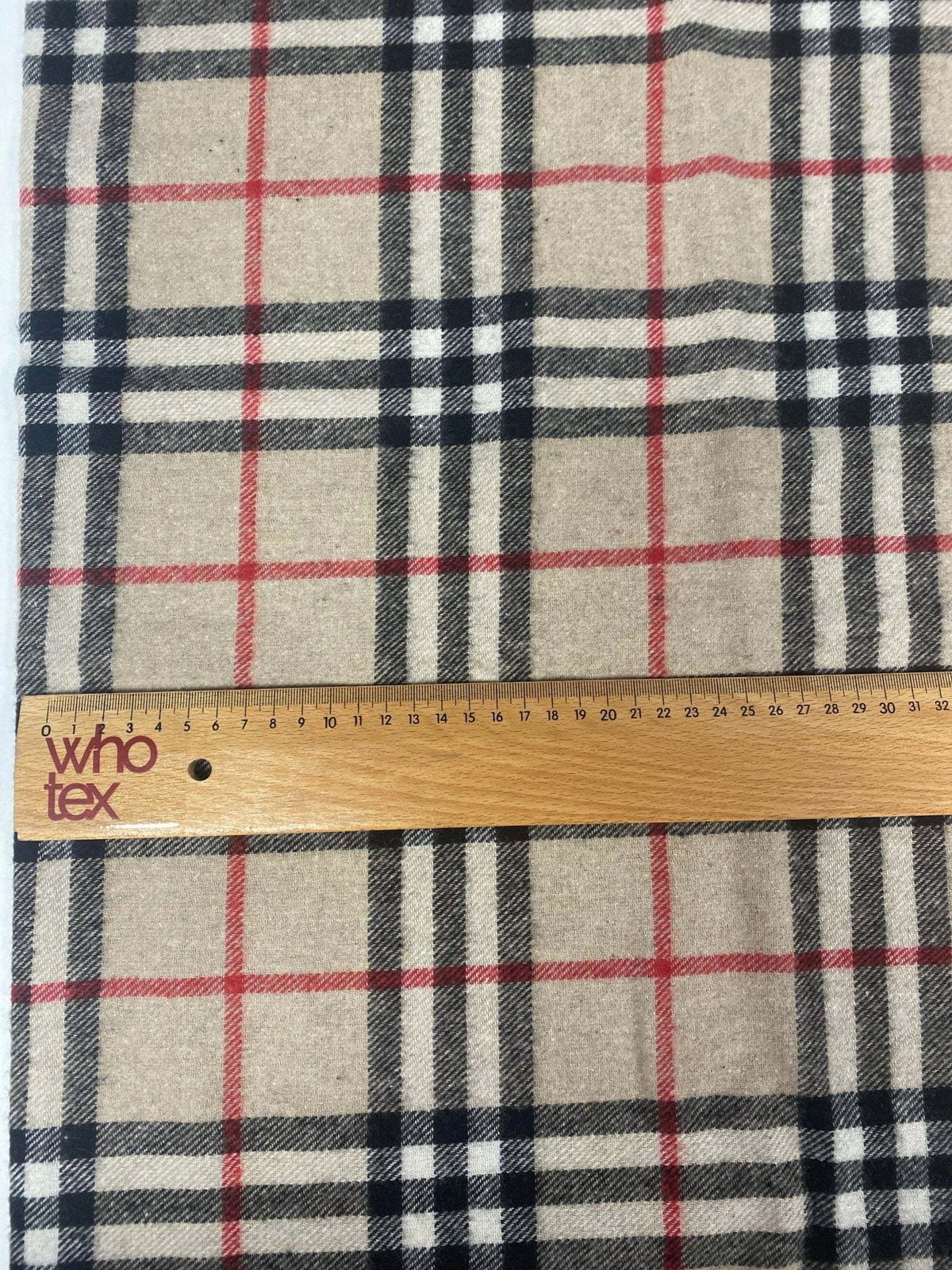 Plaid woolen fabric with beige, black, and red check pattern and wooden ruler showing scale