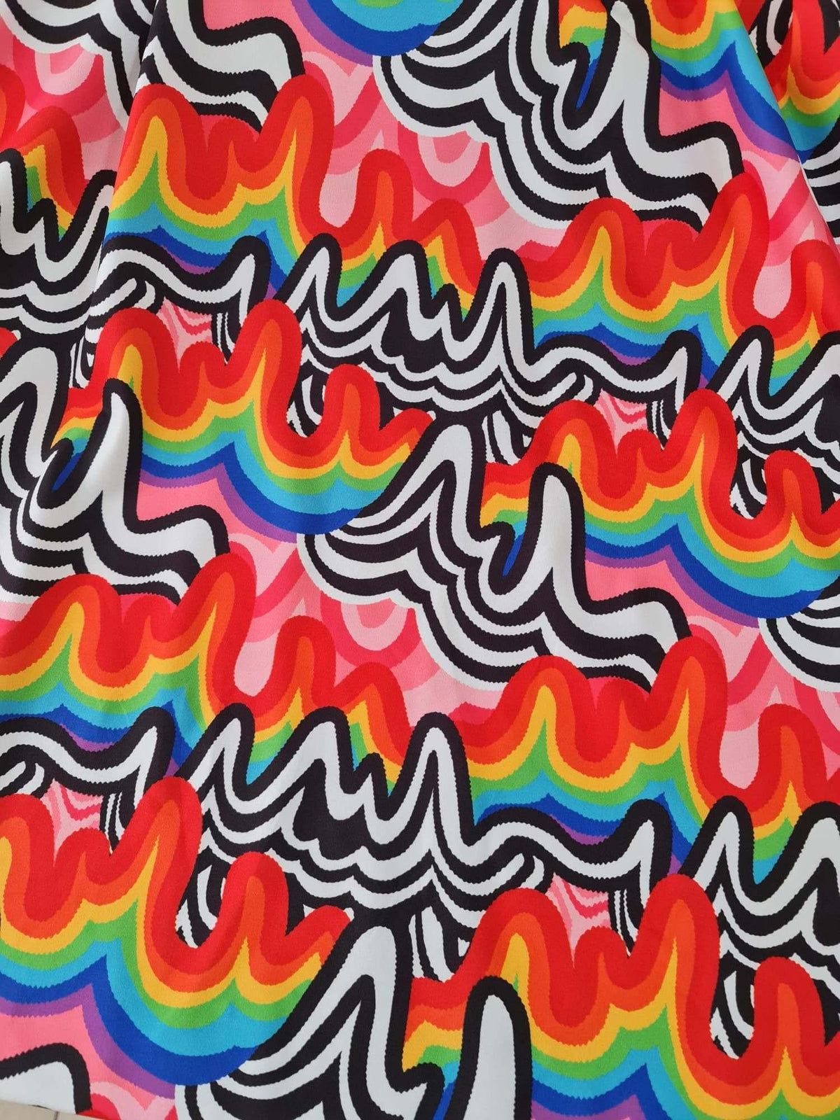 Close-up of vibrant rainbow abstract print fabric with wavy black and white patterns on a pink background