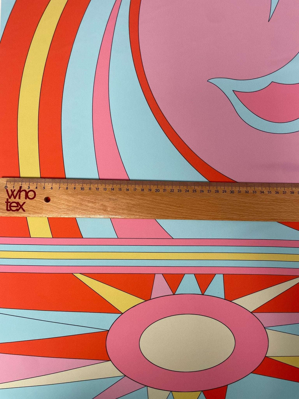Close-up of retro psychedelic swirl and sun print fabric in pink, orange, yellow, blue, and cream colors with ruler for scale