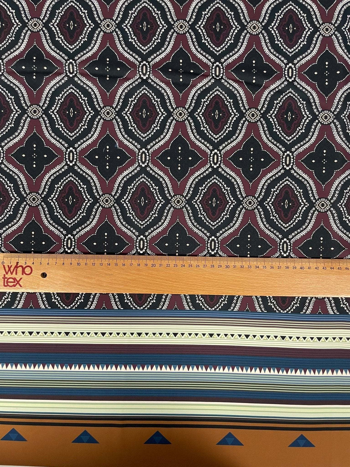 Burgundy and black geometric patterned fabric with ethnic striped edge and measuring ruler for scale