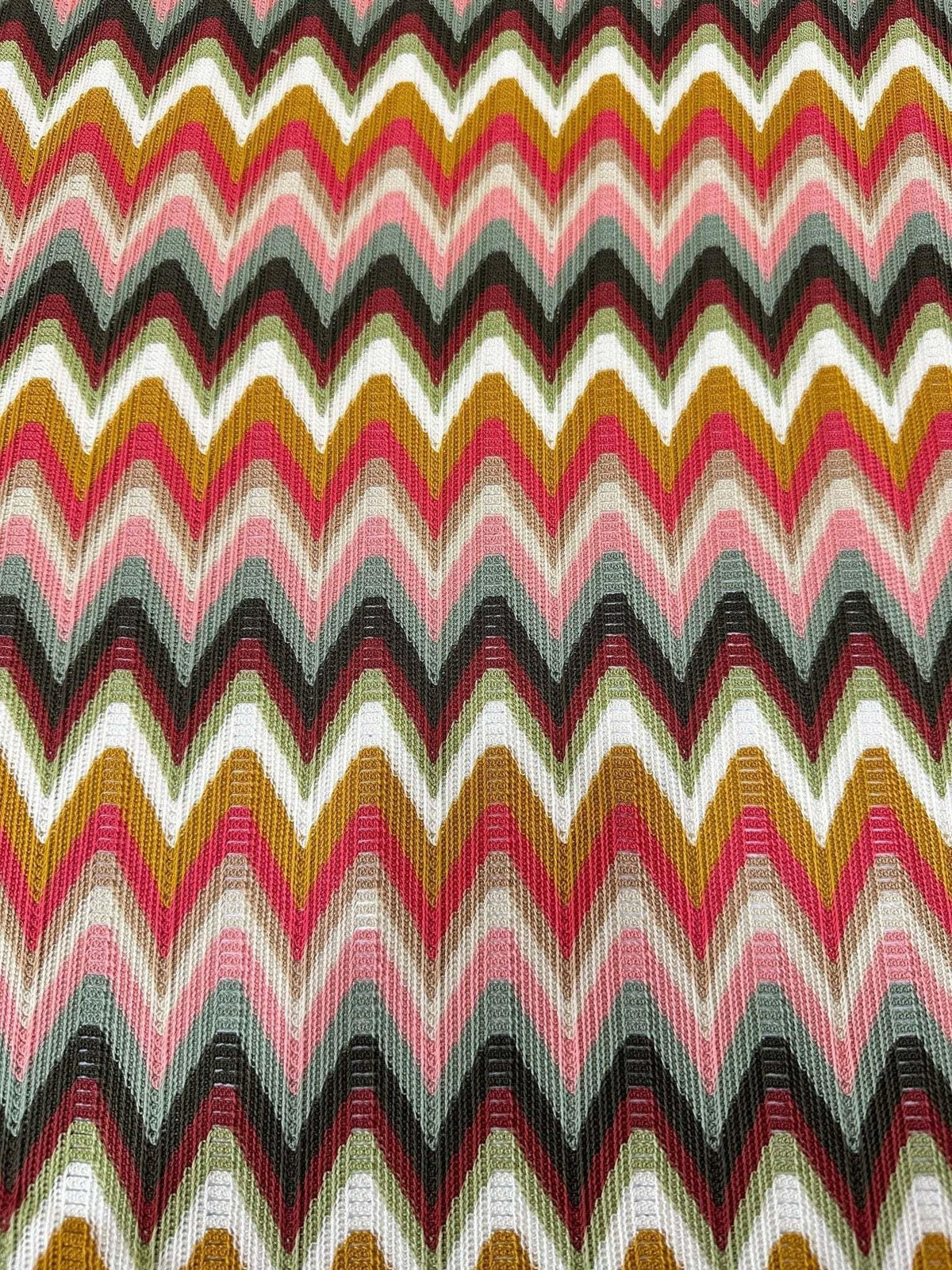 Luxury autumn chevron zigzag knit jersey fabric with warm tones of pink, mustard, black, and white, ideal for elegant autumn attire.