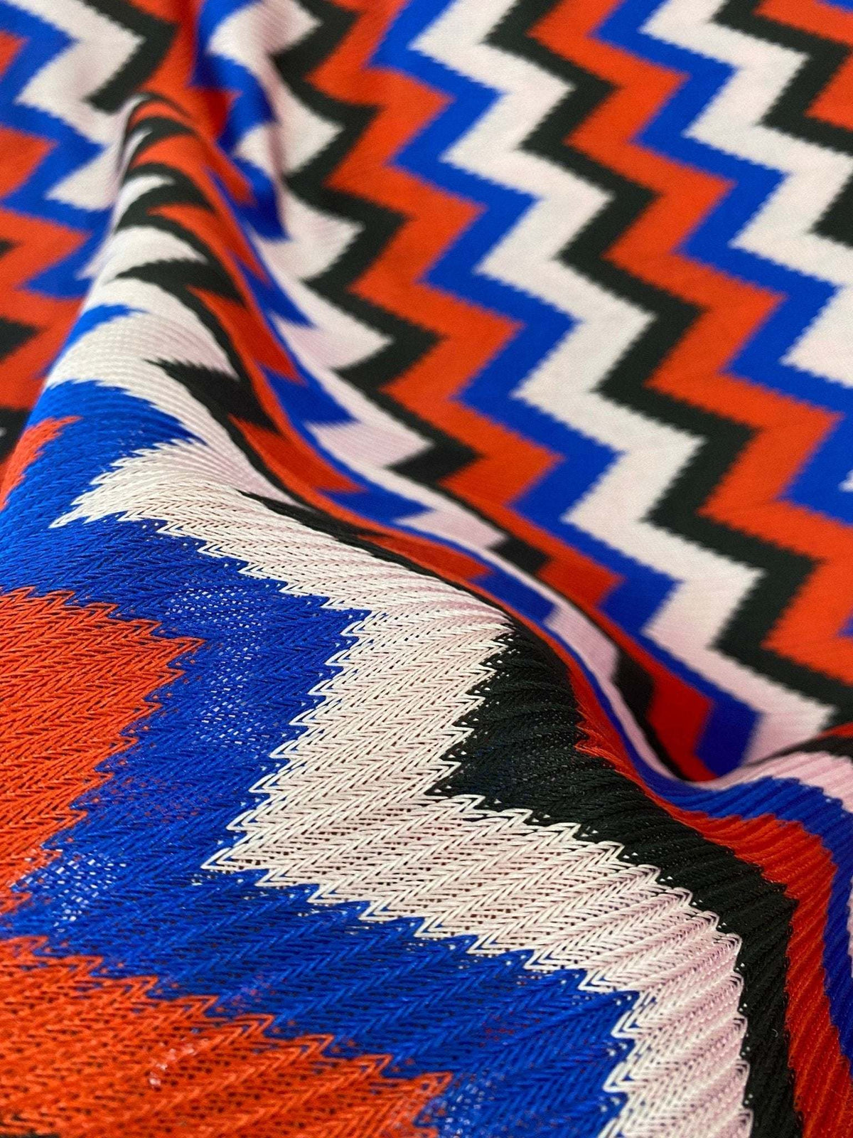 Luxury zigzag knit jersey fabric with vibrant blue, red, black, and pink zigzag pattern, soft and stretchy textile for elegant garments